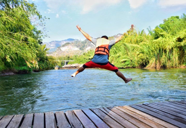 man in life jacket jumping into a lake 