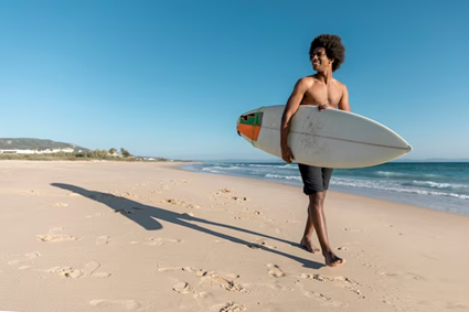 curly man on a beach with a surf board 
